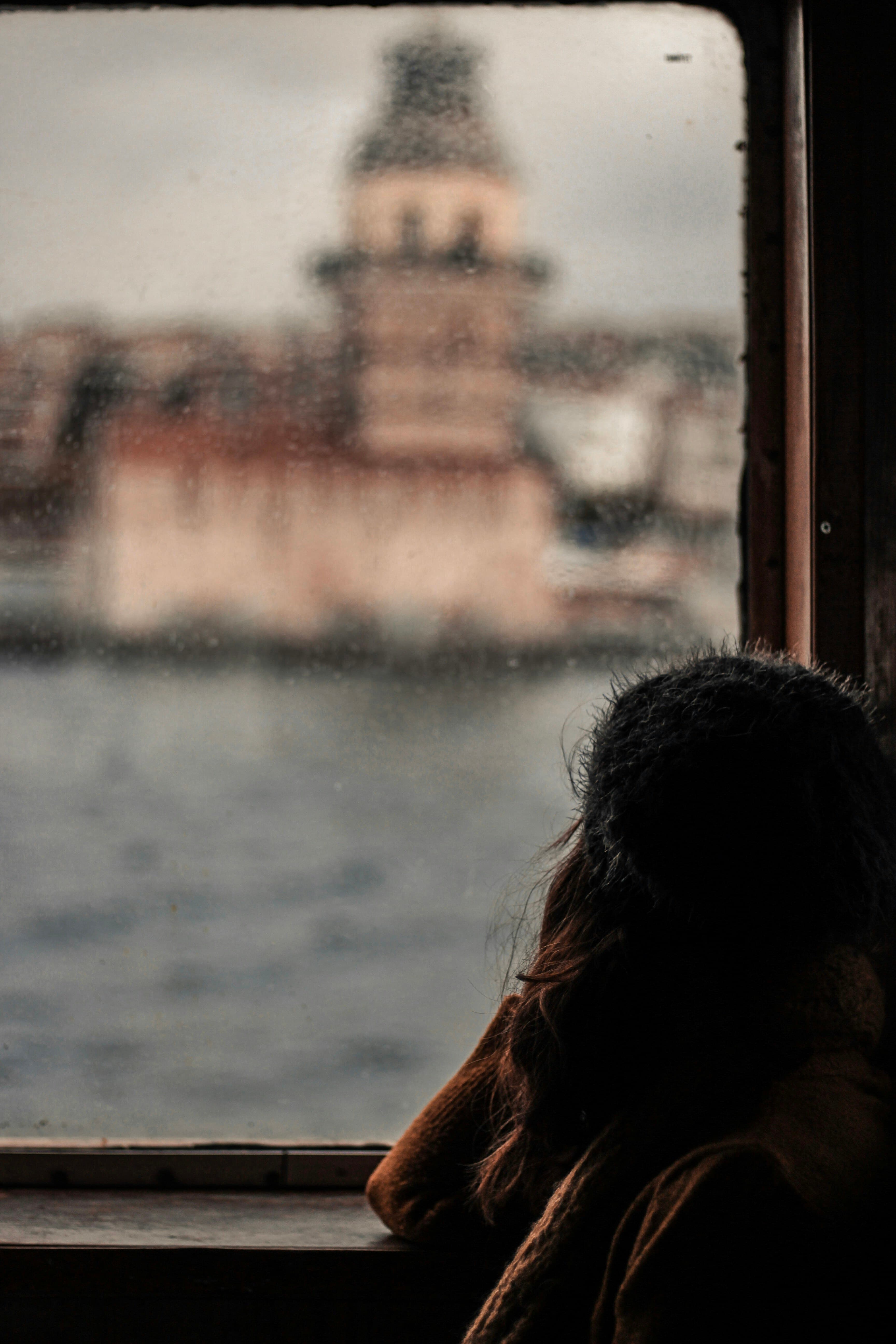 Person gazing out of a rain-streaked window with a distant, wistful expression